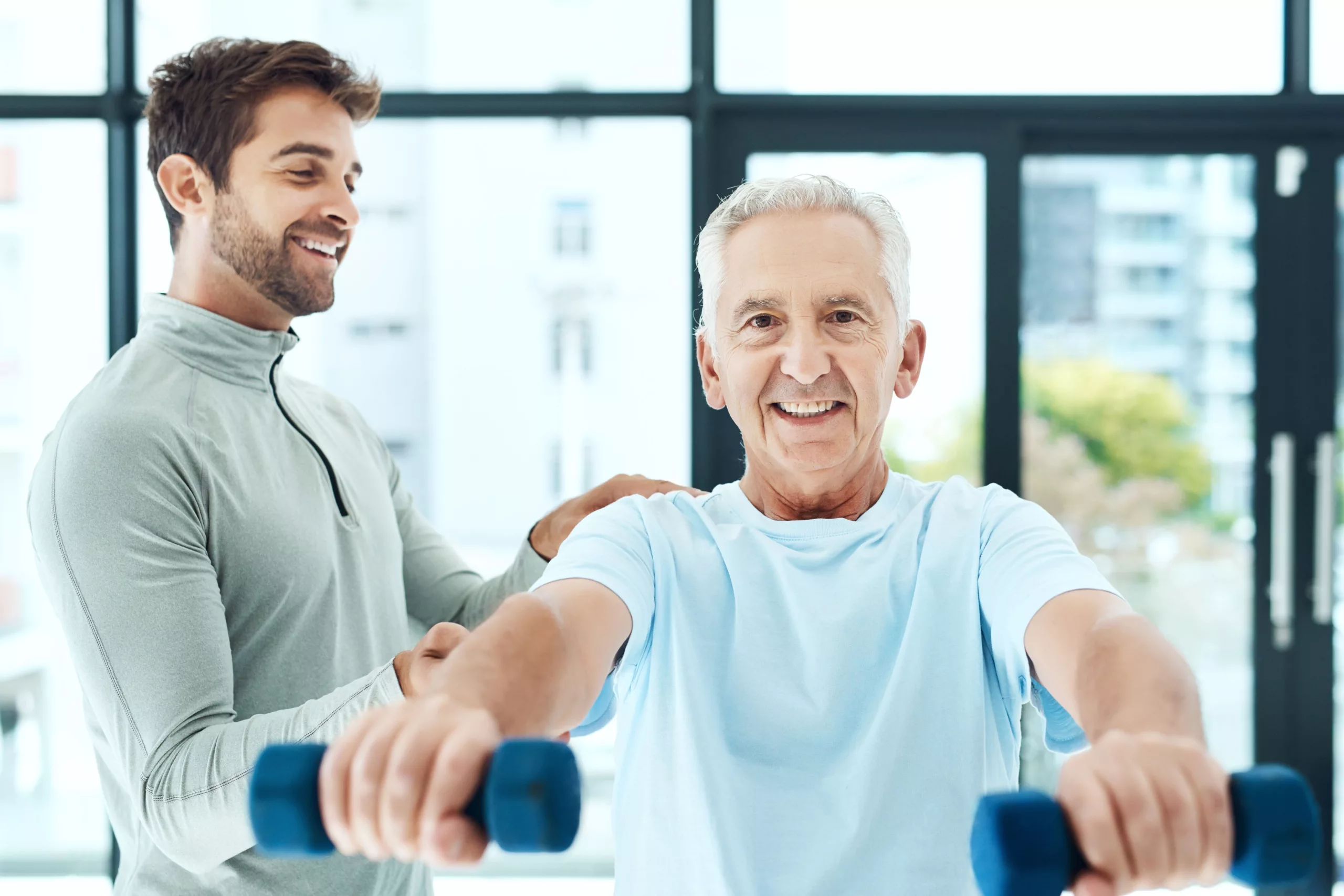 A physiotherapist helping a senior citizen client's posture while lifting dumbbells